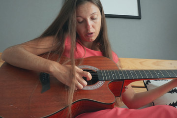 Closeup of female musician playing guitar. Young caucasian woman in red dress is practising guitar playing