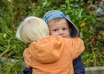 Caucasian children hugging on the street. Brothers love each other. The boy in the cap is smiling and happy . He enjoys the weather and the walk