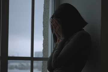 Profile Portrait Of A Sad African American Woman With Straight Black Hair In The Dark Staying Beside The Window And Close Her Face With Arms