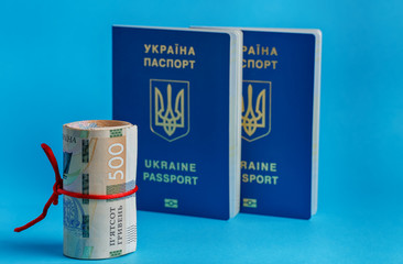 500 hryvnia roll wrapped in a red rope ribbon on the back plate 2 biometric passports of Ukraine on a blue background