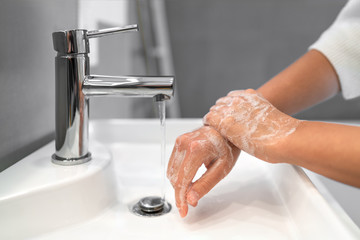 Hand washing lather soap rubbing wrists handwash step woman rinsing in water at bathroom faucet...