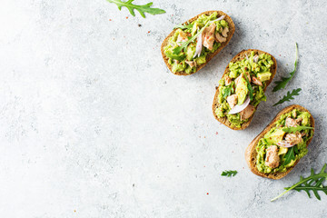 Avocado toast with tuna and arugula, overhead view. Food background with copy space.