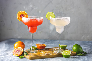 Frozen lime margarita and blood orange margarita cocktail mix in salt rimmed glasses garnished with...