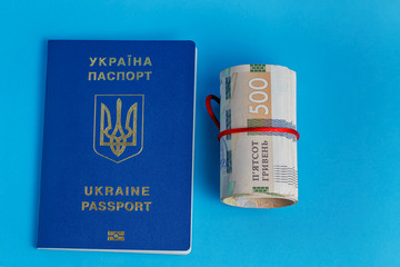 500 hryvnia roll wrapped in a red rope ribbon on the back plate 2 biometric passports of Ukraine on a blue background
