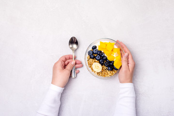 Female Hand are Holding Glass Bowl with Healthy Food Bowls of Muesl and Yogurt with Berry and Mango Top View