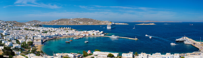 Panorama of Mykonos town Greek tourist holiday vacation destination with famous windmills, and port with boats and yachts and cruise liner. Mykonos, Cyclades islands, Greece
