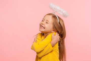 I love myself. Beautiful charming little girl with halo over head embracing herself and smiling...