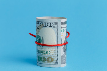 A roll of dollars wrapped in a red rope ribbon on a blue background 100 dollars