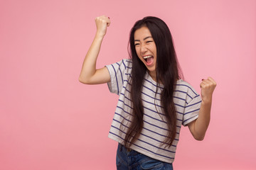 Portrait of euphoric happy joyful girl with long hair screaming with happiness and raising hands in gesture yes, hurray, I did it, celebrating victory. indoor studio shot isolated on pink background