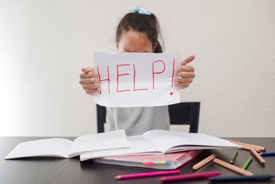 Schoolchild holding a sheet of paper with the word HELP on a white background. Concept of education and studying at home.