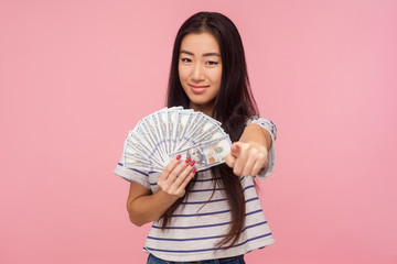 You may become rich! Portrait of beautiful girl with brunette hair pointing at camera and holding dollars, encouraging to earn money, choosing lottery winner. studio shot isolated on pink background