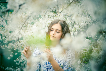 Girl in the blooming garden. Spring flowering garden. Beautiful blue-eyed girl among blossoming trees in spring