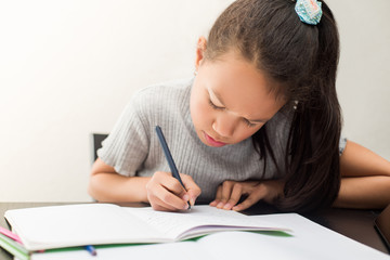 Little girl doing homework on the table. School girl writing on the notebook on a white background. Concept of education and schoolchild.