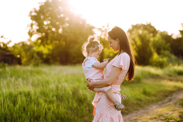 Mother and little daughter playing together in a summer park at sunset. Happy mom with small child  having fun on sunny field. Kisses and hugs. The concept of a happy family.  © maxbelchenko