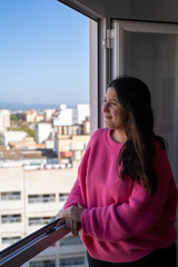Fototapeta na wymiar Woman with a pink sweater smiling and leaning against an open window