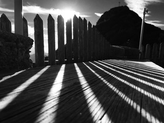 Sonne scheint durch rustikalen Zaun und wirft lange Schatten über einen Tisch vor einem dunklen...