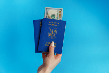 2 passports of Ukraine in the hand of a girl with manicure on a blue background inside the passport banknote 100 dollars