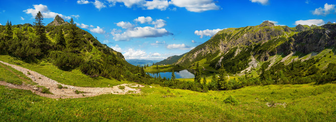 Fototapeta na wymiar Gorgeous mountain range surrounding a lake, with deep blue sunny sky and green meadows in the foreground
