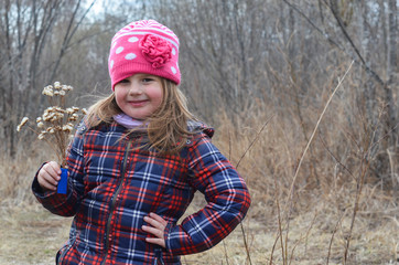 Cute caucasian little girl in late autumn in nature with a bouquet of dried flowers