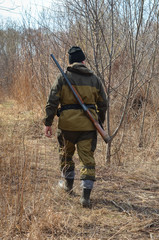 The hunter goes through the forest with a rifle on his back rear view. A man on the hunt