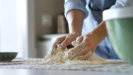 Obraz na płótnie Canvas Authentic close up shot of an young woman with apron is kneading a dough for pizza or pasta preparation for lunch in a kitchen. Concept of housewife, cooking, traditional italian food, authenticity