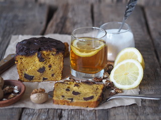 Tea party with festive pumpkin chocolate soft muffin, poured with chocolate icing on parchment paper with walnuts on a wooden ancient background.Homemade baking.