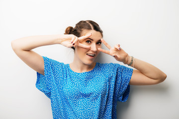 Portrait of cheerful young woman showing two fingers or victory gesture, over grey background