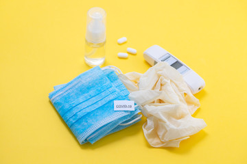 medical mask, gloves and disinfectant on yellow background