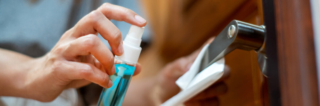 woman hand disinfecting the door handle by spraying a blue sanitizer from a bottle for Covid-19 Coronavirus prevention.