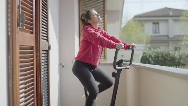 Cheerful girl pedaling on exercise bike on balcony