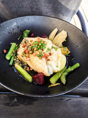 Piece of white fish, served with asparagus, beets, bacon and chives, in a black rustic bowl.