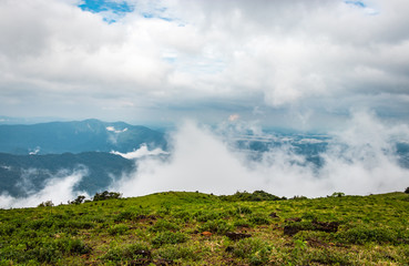 Fototapeta premium Cloud layers on mountain horizon with green grass