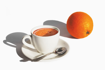 White cup of coffee and an orange on white background with hard shadows of morning light. Best start to the day. Copy space.