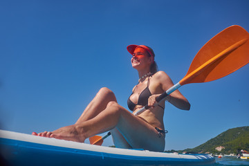 Side view picture of a woman sitting and relaxing on the sup board. Surfer woman resting