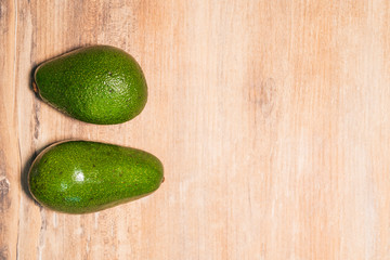 Two fresh green avocados on a wooden table, top view. Copy space for your text