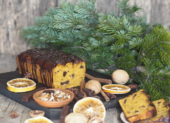 Festive Christmas food background. Holiday pumpkin chocolate soft muffin, poured with chocolate icing, with ingredients and fir branches on a wooden background.