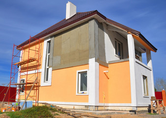 Painting renovation a modern house with stucco house finish, stucco siding and metal roof using scaffolding.