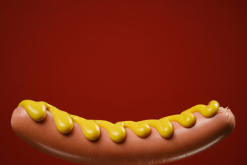 sausage with mustard on a black fork, red background, isolated