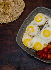 fried eggs with sausages and cherry tomatoes in a grill pan, beautiful simple breakfast, breakfast on a dark wooden table, close-up