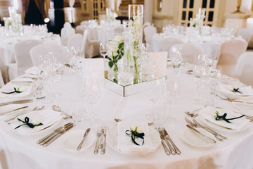 Wedding decorations. On the tables in the banquet hall are compositions of vases with water and white flowers, plates with napkins, candles and glasses