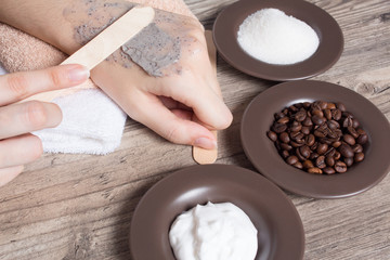 A woman puts a spatula of coffee homemade scrub on her hand. SPA, beauty. Ingredients for making scrub, coffee beans, sugar, cream. Skin care.  Moisturizing, exfoliating, peeling. Home Cosmetics, Eco
