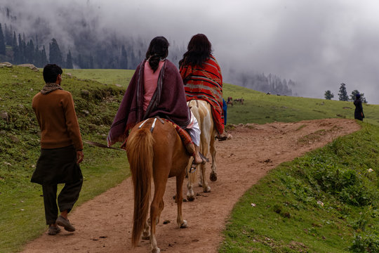 Females horse riding with male trainer in the green grass field at overcast weather