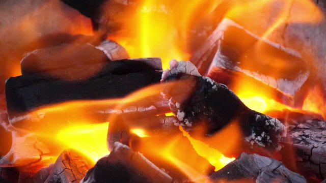 Slow motion speed closeup scene on burning charcoal pile with ash and flake of spark scattered blowing up, mirage illusion movement from hot air stream, bright orange color light of live coal