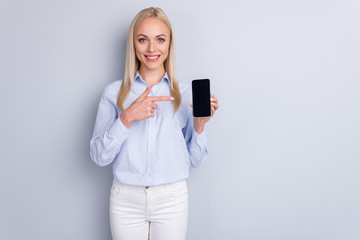 Naklejka premium Portrait of positive cheerful promoter girl hold new smartphone device point index finger suggest select wear good look trousers isolated over gray color background