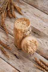 Fototapeta na wymiar Wheat natural leaven for bread in a glass jar. A living product. Spikelets. The concept of a healthy diet. Sourdough starter. Copy space, vertical banner