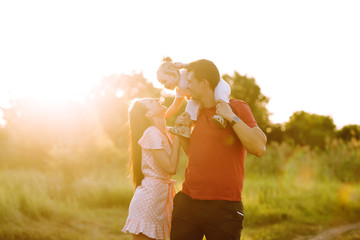 Happy young family walking in the park at sunset. Mom, dad and little daughter having fun in summer...