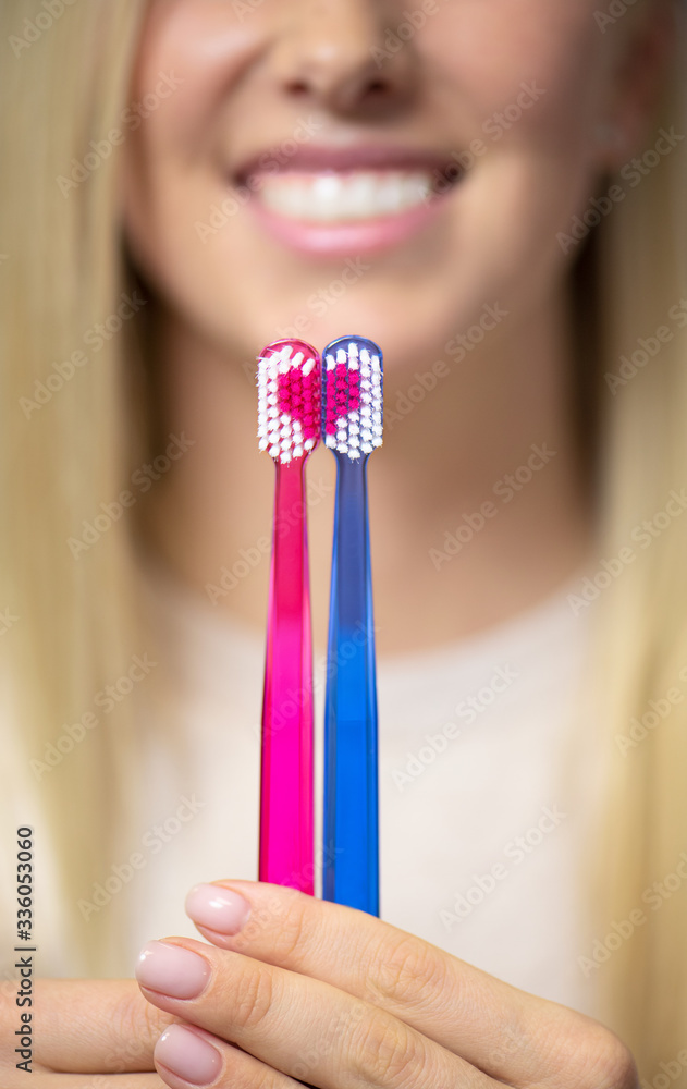 Wall mural Woman showing toothbrushes forming a heart symbol, vertical photo