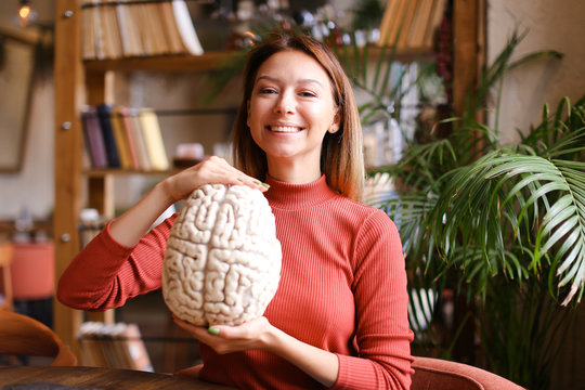 Female smiling psychologist holding human brain model at cabinet.
