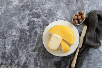 cheese on white plate and olives in small bowl on dark background