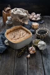 Raw dough for whole grain Danish bread with garlic rising in ceramic form on baking paper, sprinkled with seeds. ingredients for baking bread. Atmospheric image for Cook book. Yeastless bread recipes
